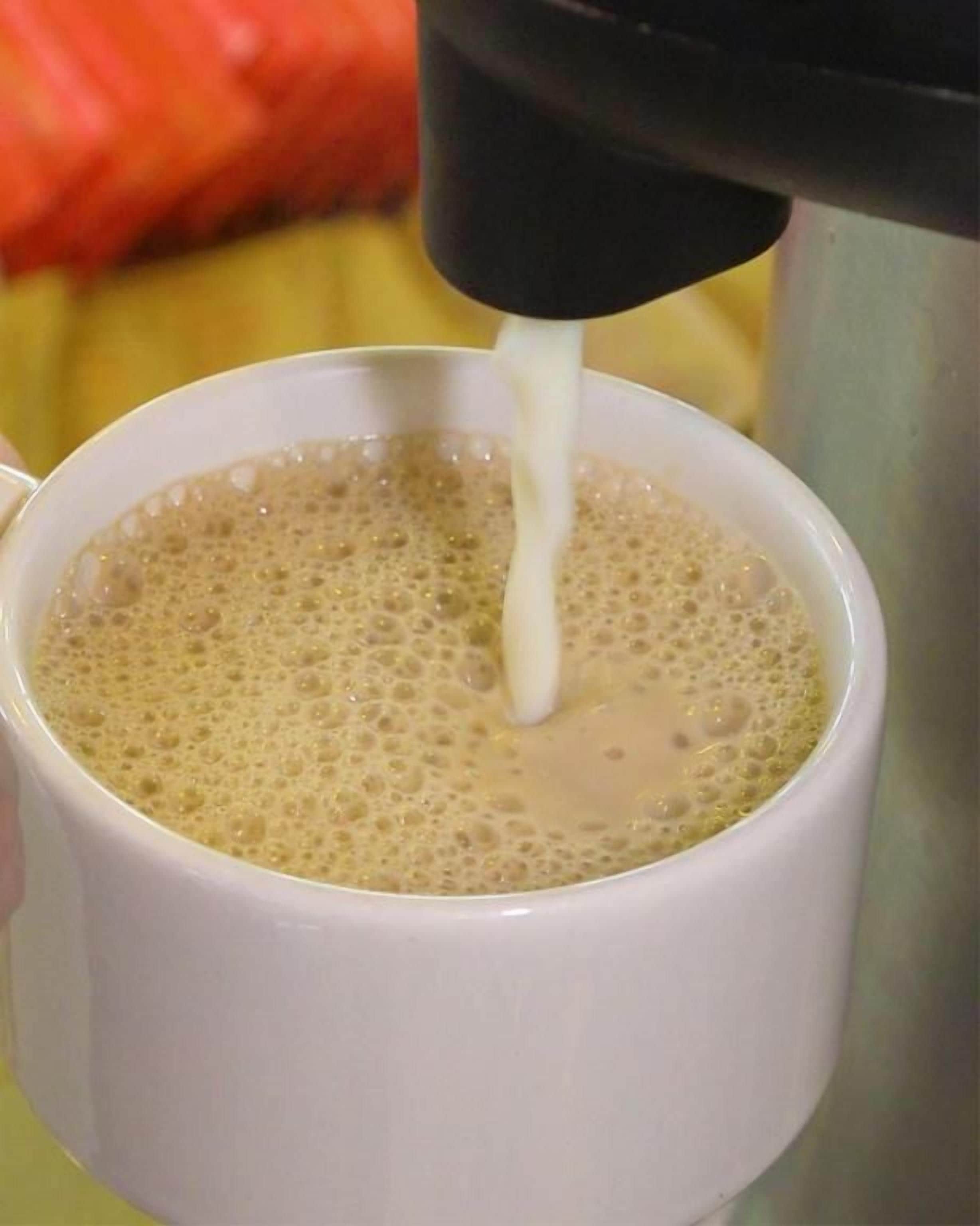 Una tazza che viene riempita con una bevanda spumosa, probabilmente caffè o tè, da una macchina.
