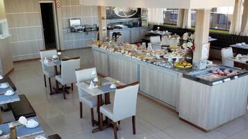 Comedor de hotel con barra de buffet, mesas dispuestas y cocina al fondo.