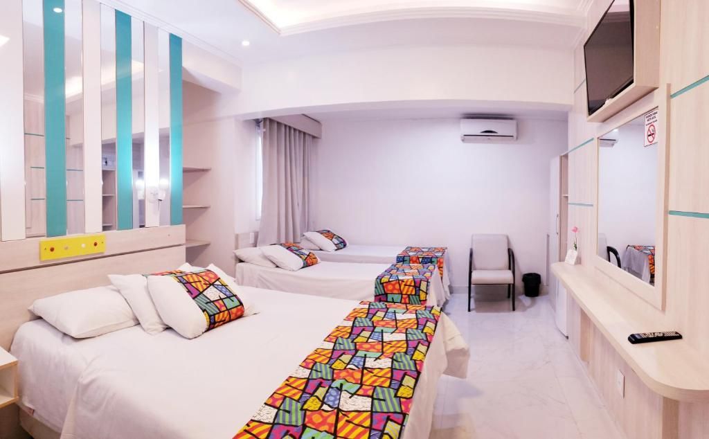 A hotel room with two beds, a desk, a chair, a TV, and a bathroom.