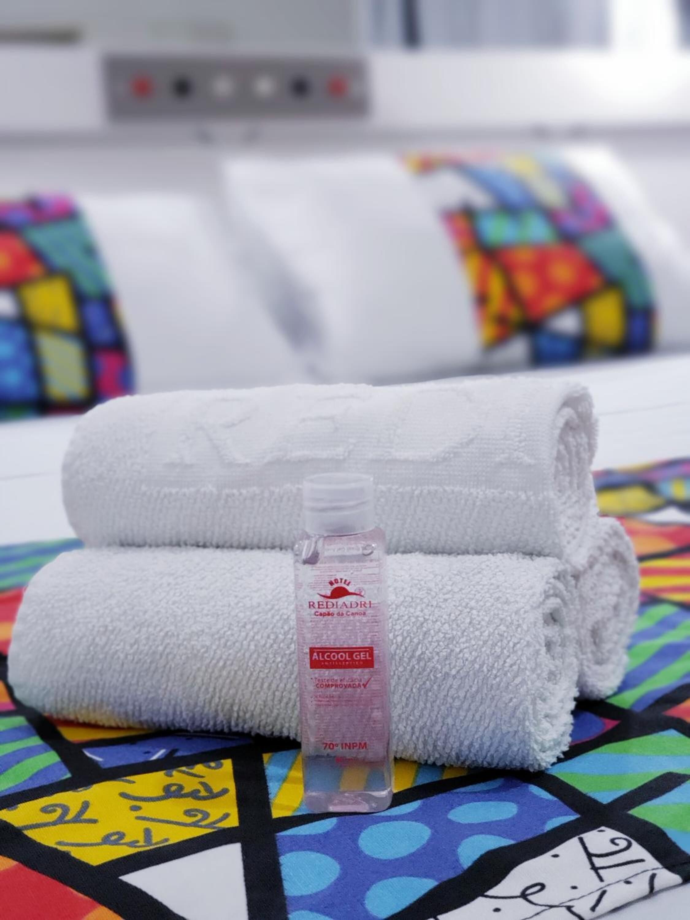 Ein ordentlich gefaltetes weißes Handtuch mit einer Handdesinfektionsmittel-Flasche in der Mitte, platziert auf einer farbenfrohen, gemusterten Tagesdecke.