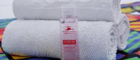 Una toalla blanca doblada con cuidado y un dispensador de gel antibacterial en el centro, sobre una colcha de colores y estampados.