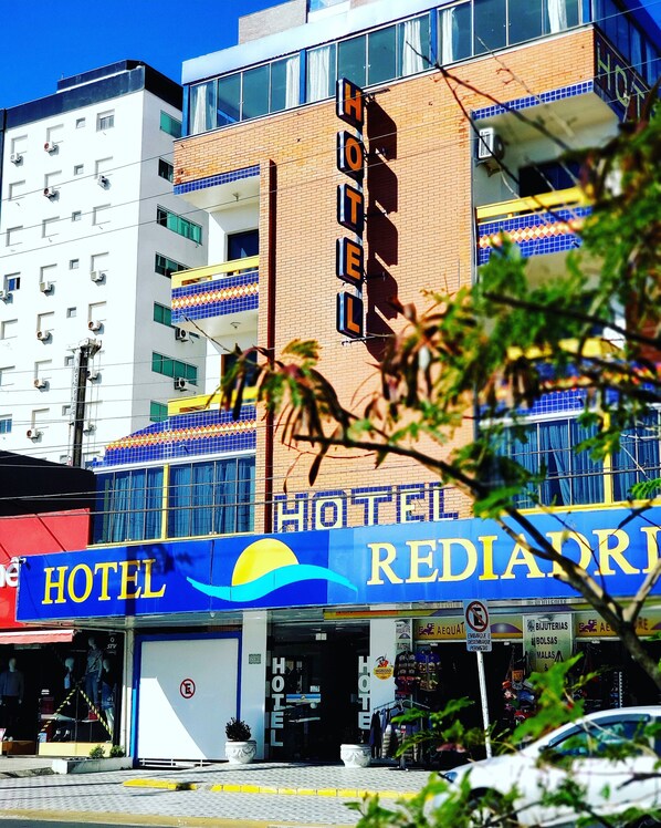 Un hôtel avec une enseigne bien visible portant l’inscription « HÔTEL REDIADR » et un grand logo représentant un soleil et une vague.