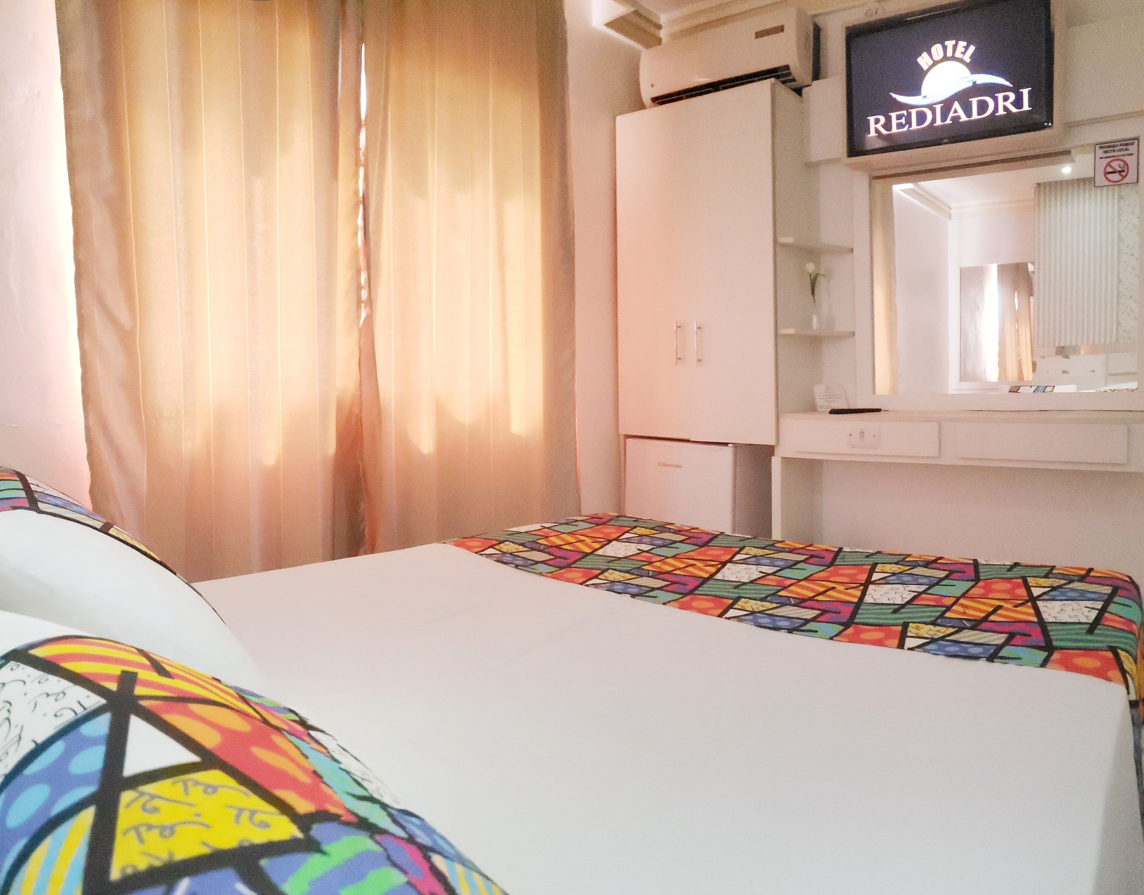Een hotelkamer met een bed, een kledingkast, een bureau en een bord met de naam van het hotel.