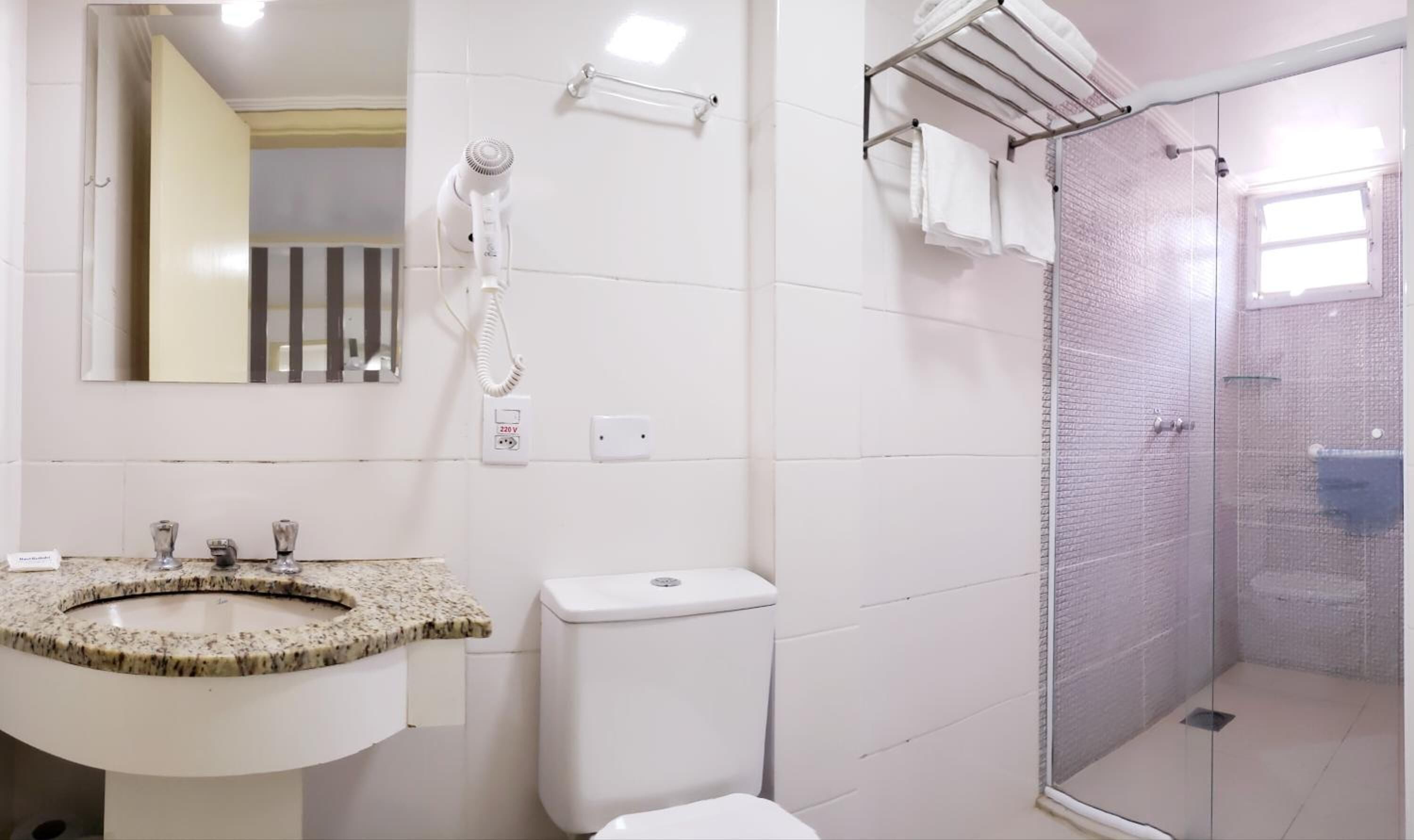 A bathroom with a granite sink, a toilet, a shower with a glass door, and a towel rack.