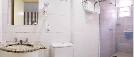 Un baño con lavamanos de granito, inodoro, ducha con puerta de vidrio y toallero.