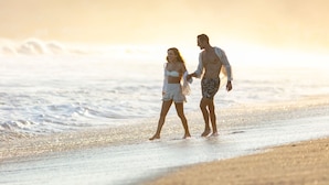 Una pareja caminando por la playa, con olas al fondo.