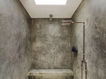 Shower area with a minimalist design, featuring a textured concrete wall and a visible water pipe system. at Drift San Jose del Cabo, a Member of Design Hotels