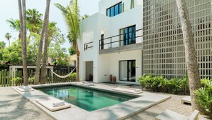Un área de piscina moderna con una piscina rectangular, escalones de hormigón y una hamaca.