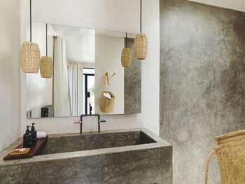 Bathroom features a large sink, shower curtain, and window, with wicker baskets and a towel rack. at Drift San Jose del Cabo, a Member of Design Hotels