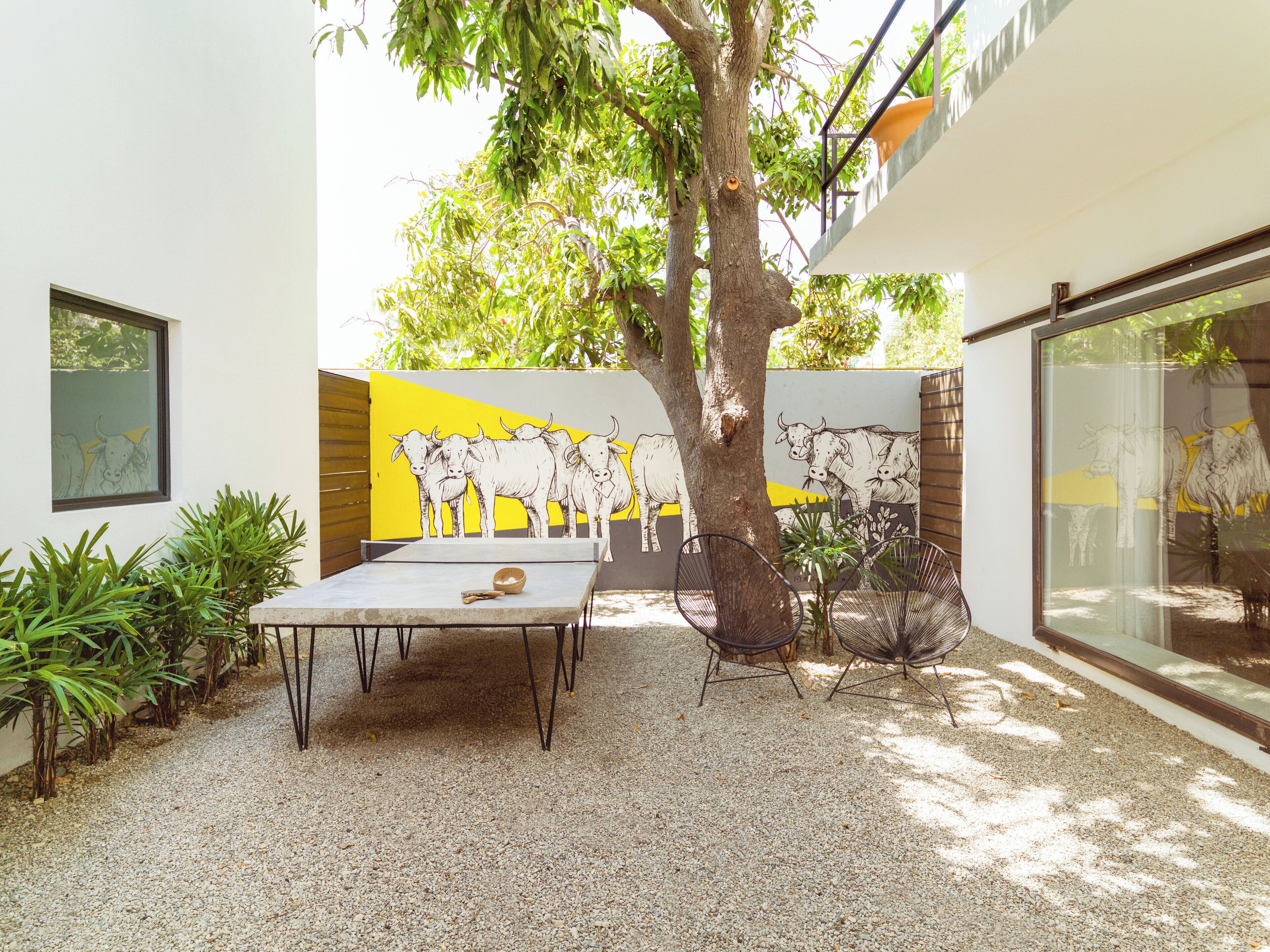 Un patio con una mesa y sillas, un árbol y un mural de toros en la pared.