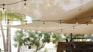 Un patio al aire libre con mesas y bancos de madera, luces colgantes y una zona de bar.