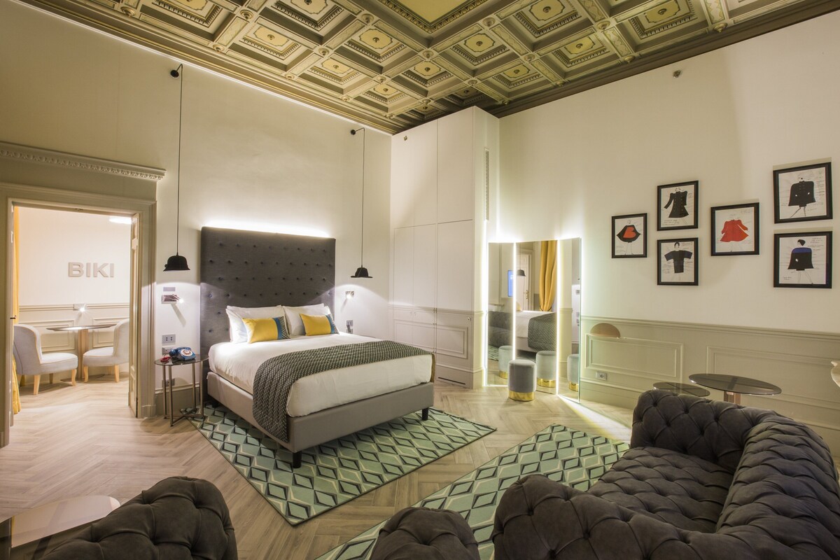 A modern hotel room with a large bed, a sofa, a desk, and a dining area.