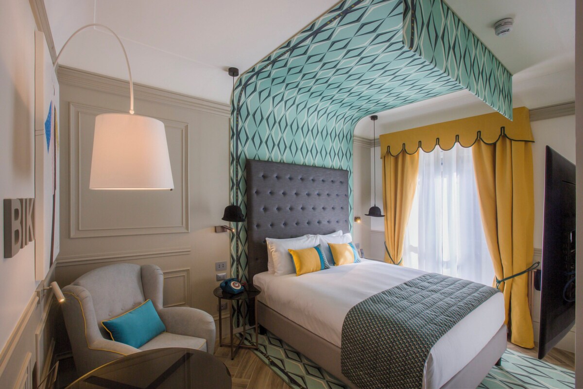 Een hotelkamer met een bed, een stoel, een nachtkastje, een lamp en een televisie.