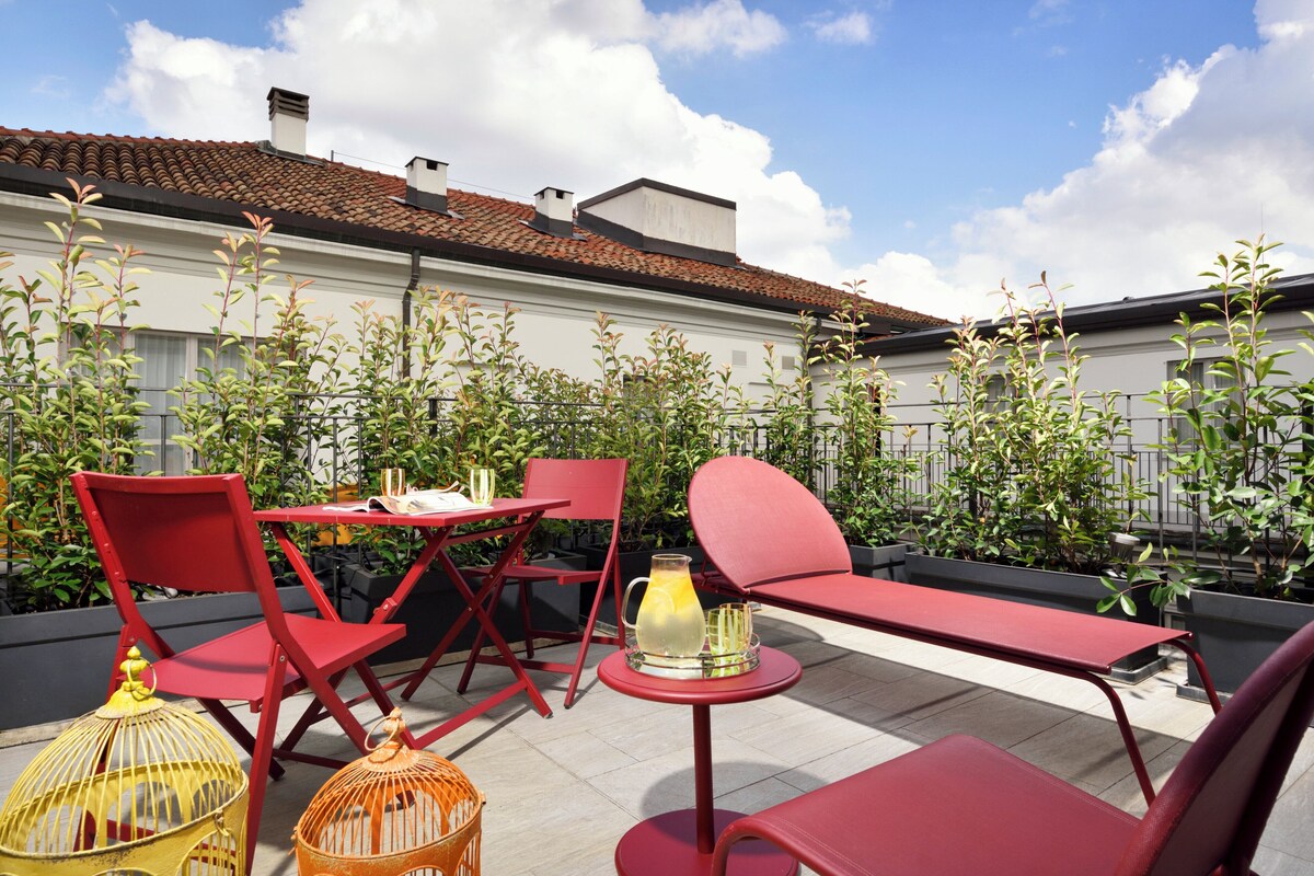 Eine Terrasse im Freien mit roten Metallmöbeln, einem Tisch mit einer Limonadenkanne und Topfpflanzen.