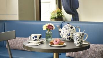 A round table with a teapot, cups, a vase with flowers, and a plate with pastries.