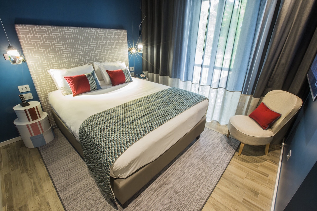 A neatly arranged hotel room with a large bed, a chair, a nightstand, and a wall-mounted TV.