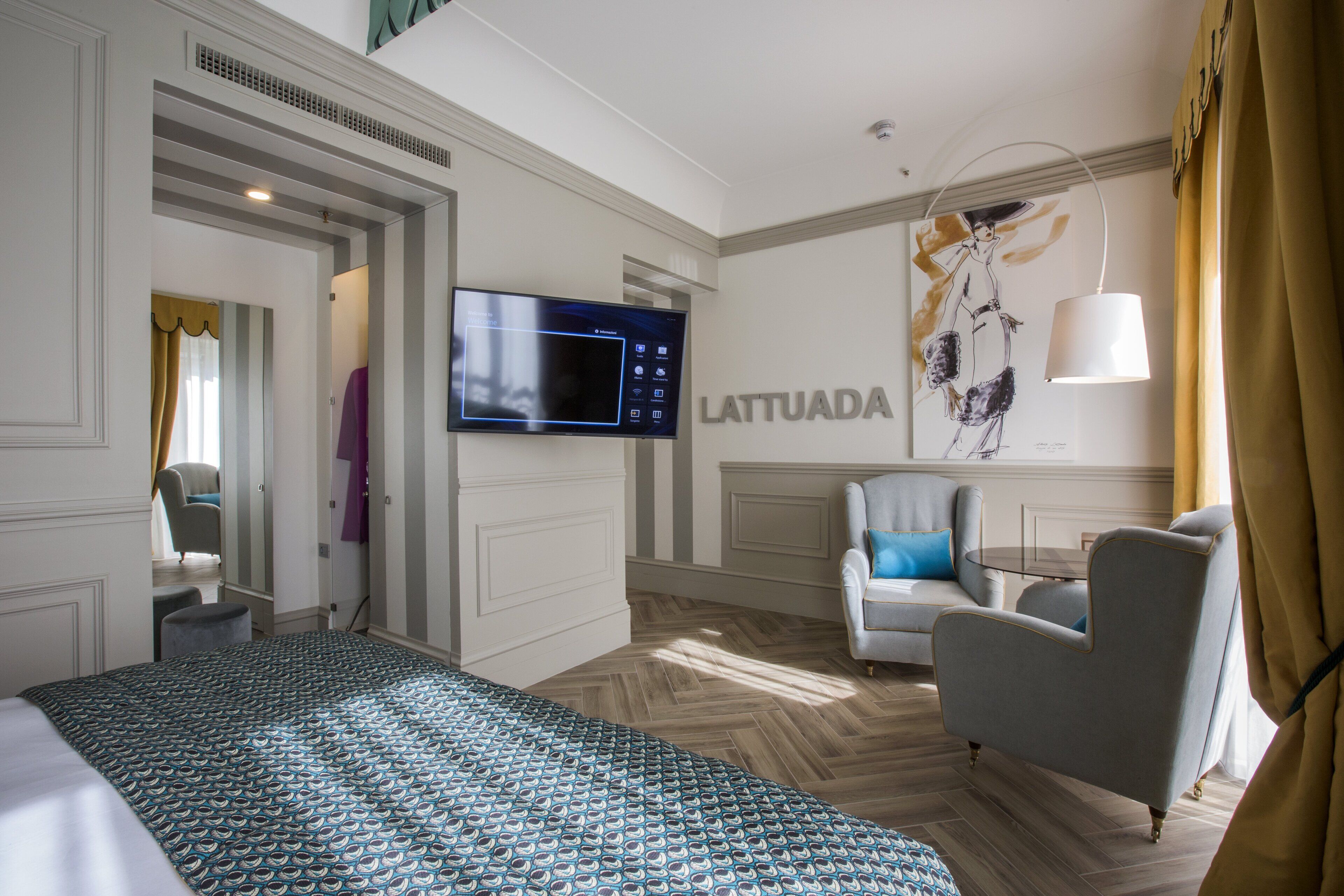 A hotel room with a bed, a television, a chair, a sofa, and a wall with the word "LATTUADA".