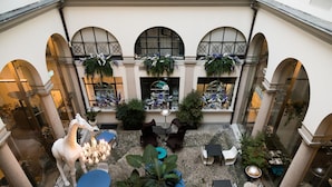 A courtyard with a statue, tables, chairs, and hanging plants. - Hotel Indigo Milan - Corso Monforte by IHG (Milan)