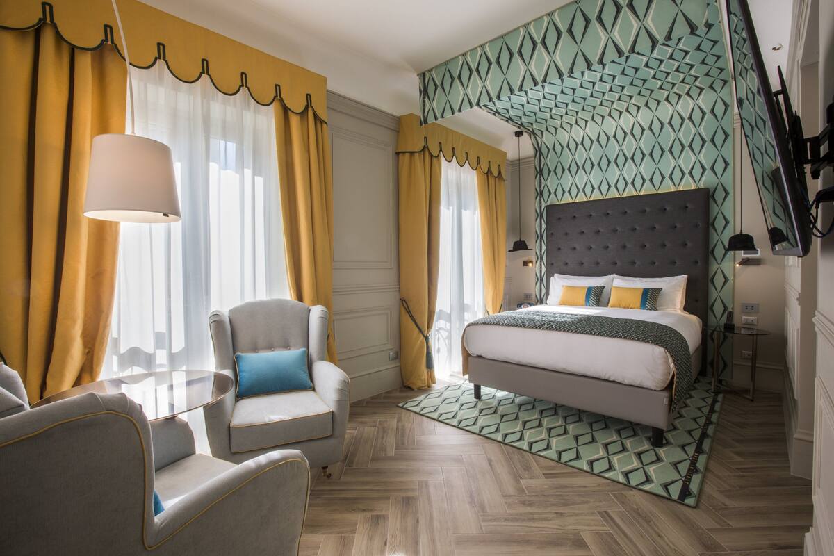 Een hotelkamer met een bed, een stoel, een tafel en een behang met patroon.