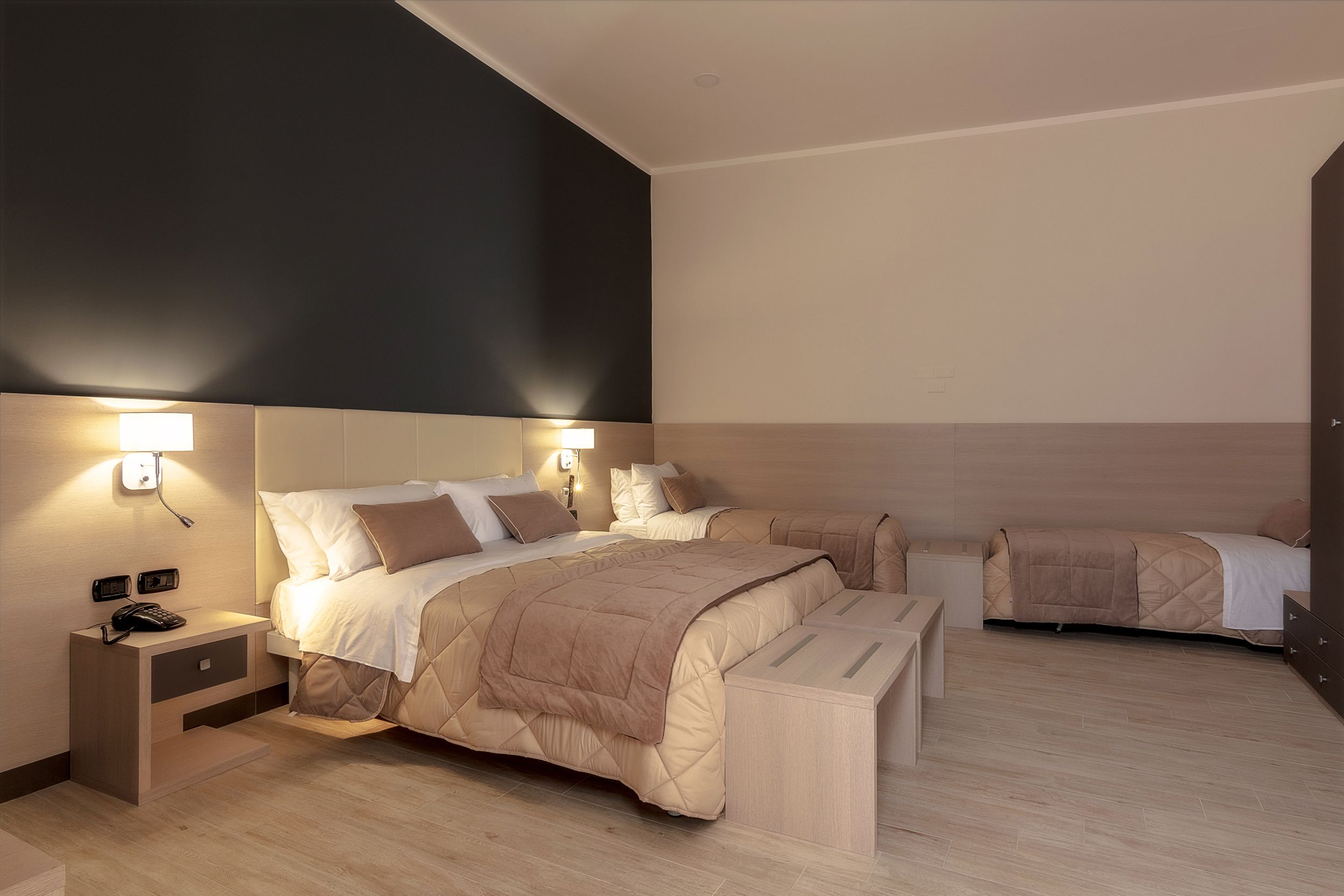 Quarto de hotel moderno com cama grande, mesas de cabeceira e iluminação embutida na parede.