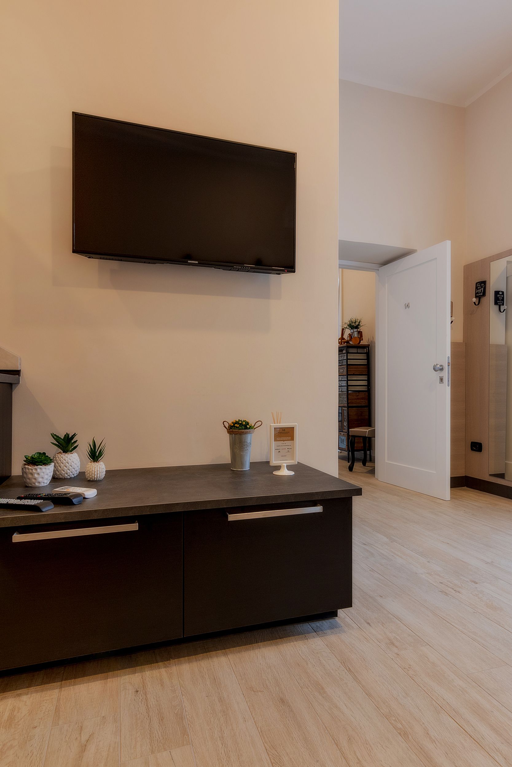 Una sala de estar moderna con un televisor de pantalla plana montado en la pared, un mueble de madera oscura con cajones y una pequeña planta en maceta sobre el mueble.