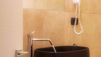 Une salle de bain moderne avec un lavabo noir, un porte-serviettes et un sèche-cheveux fixé au mur.