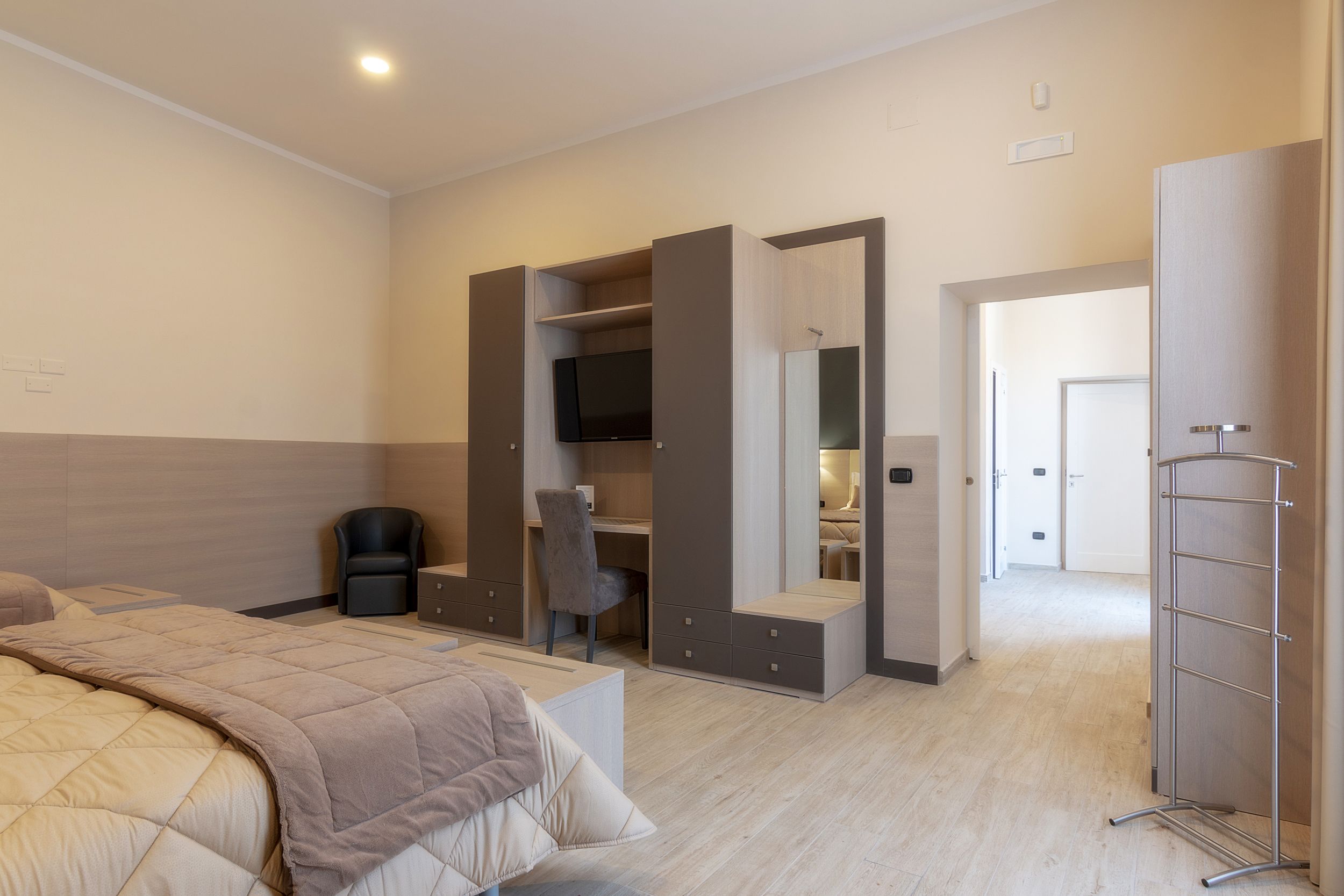 A modern bedroom with a bed, a desk, a chair, a wardrobe, and a TV.