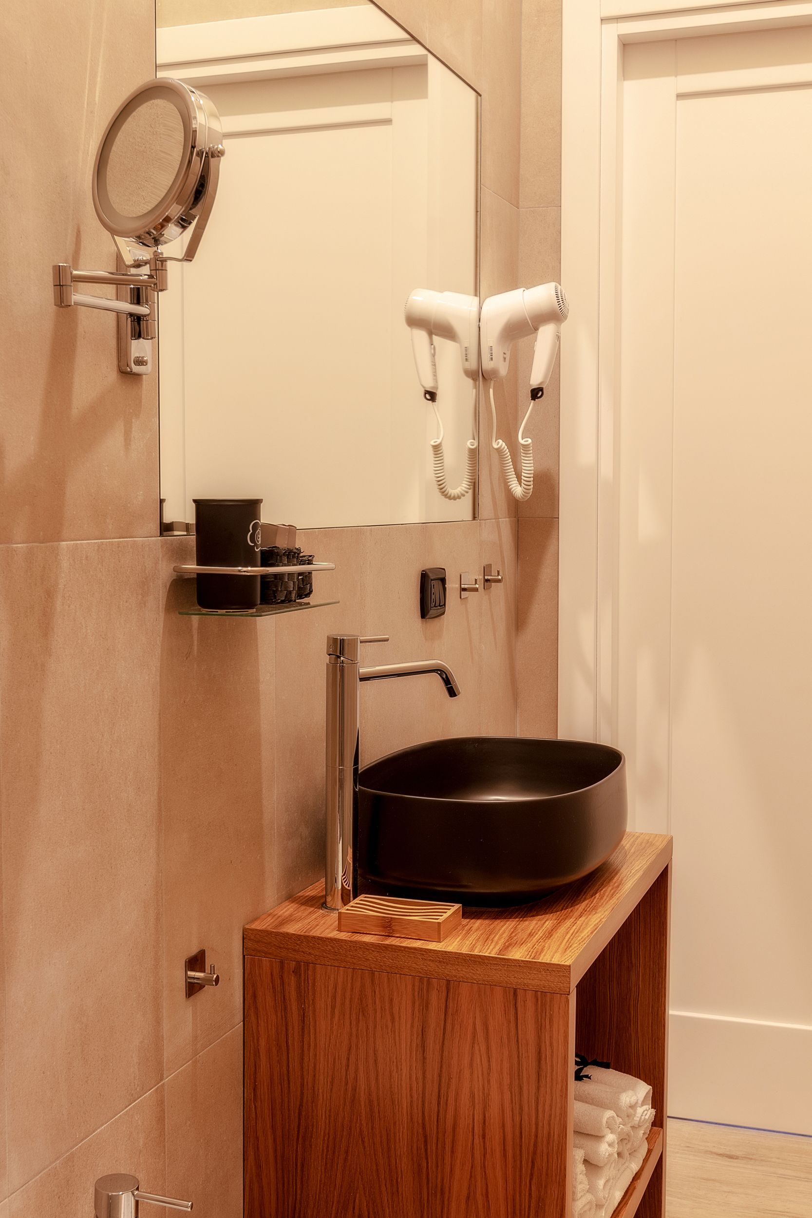 A bathroom with a wooden vanity, a black sink, a mirror, a hairdryer, and a towel rack.