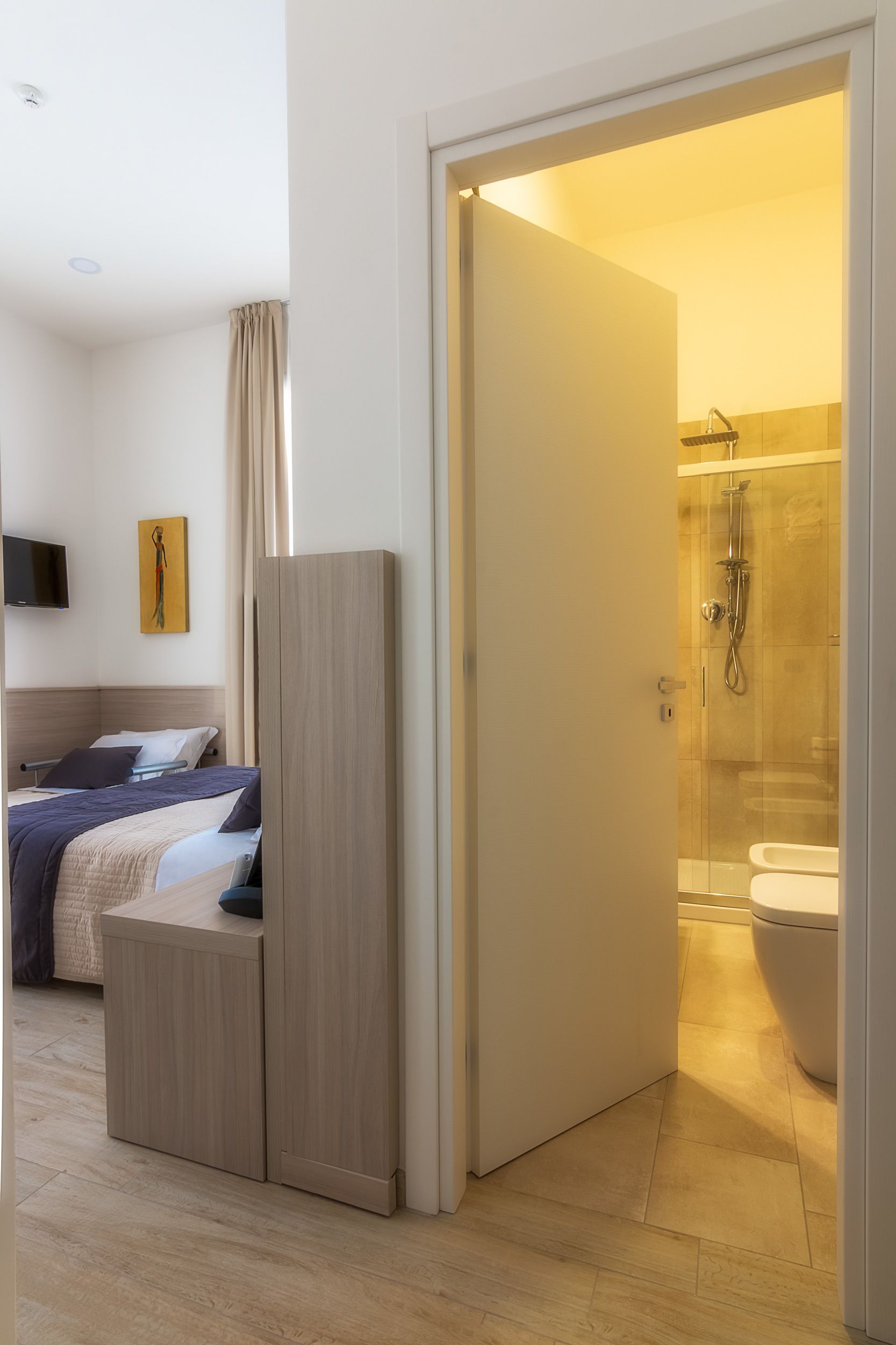 Et moderne hotelværelse med seng, garderobe og badeværelse med bruser og toilet.