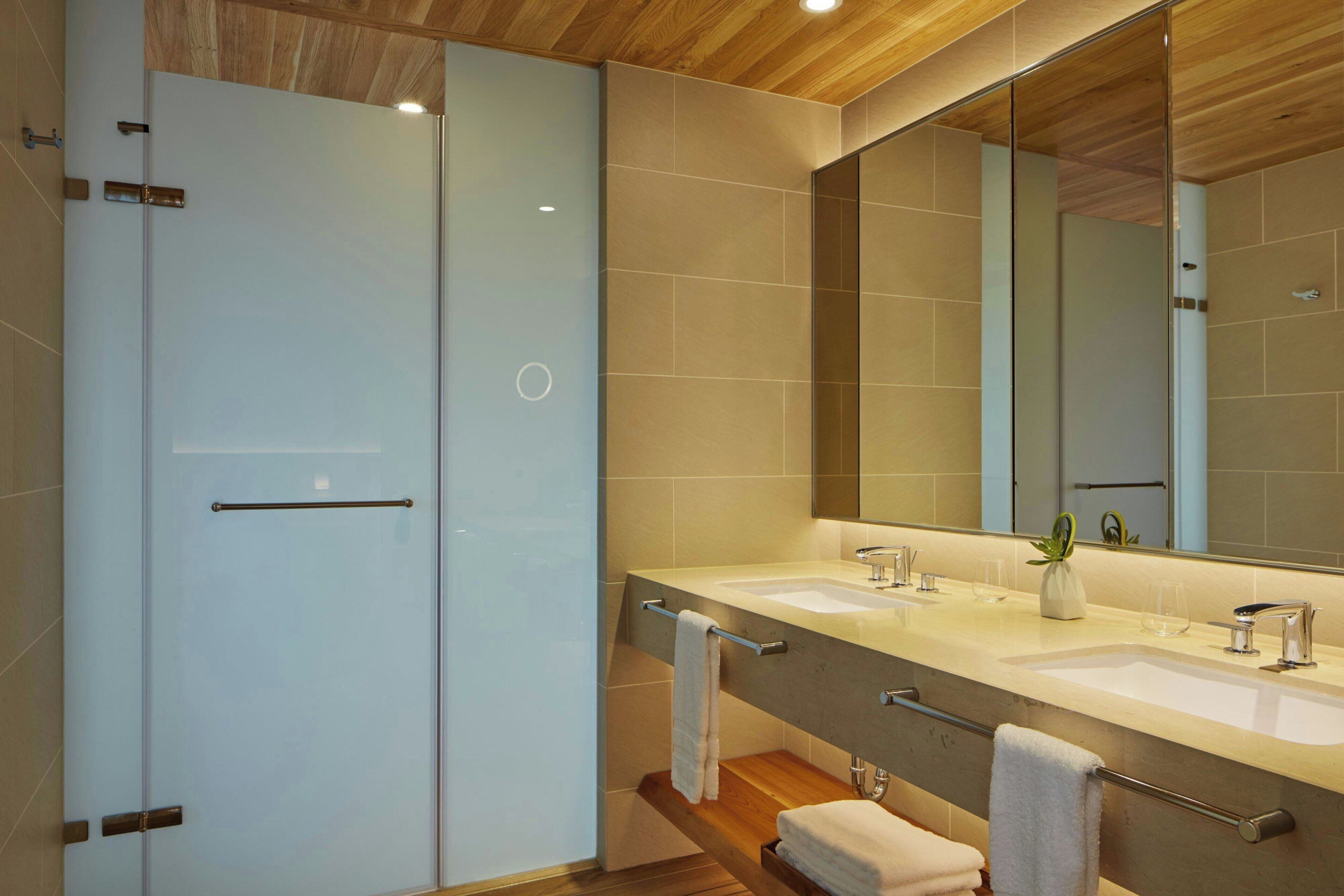 A modern bathroom with a glass shower enclosure, a double sink vanity, and a large mirror.