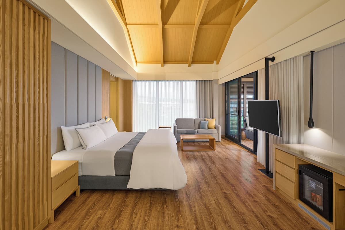 A modern hotel room with a large bed, a sofa, a TV, and a fireplace.