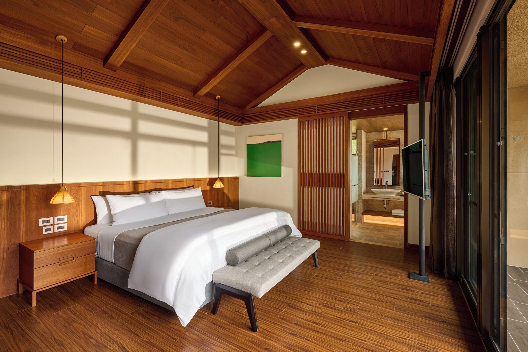 A modern bedroom with a wooden ceiling, a large bed, a bench, a nightstand, and a TV.