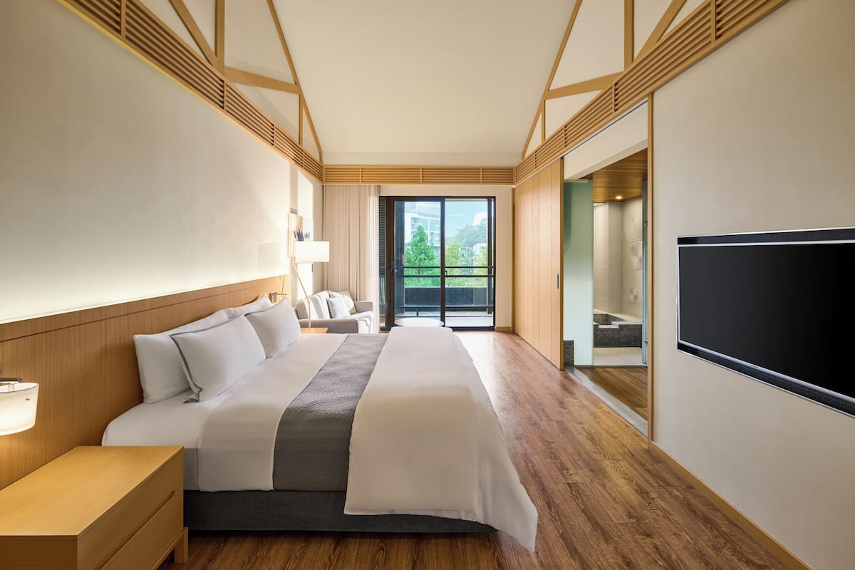 A modern hotel room with a large bed, wooden flooring, a TV, and a balcony with a view.