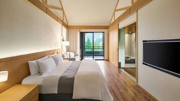 A modern hotel room with a large bed, wooden flooring, a TV, and a balcony with a view.