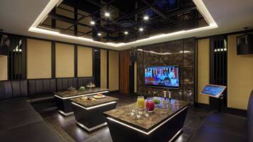A modern lounge area with a central bar, seating, and a television screen.