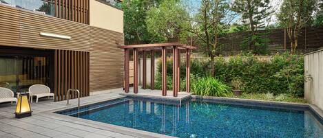 A modern outdoor pool area with a wooden pergola, a lounge chair, and a small table.