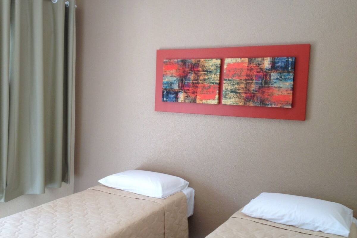 Une chambre d’hôtel avec deux lits simples, des murs de couleur beige et un tableau abstrait rouge au-dessus des lits.
