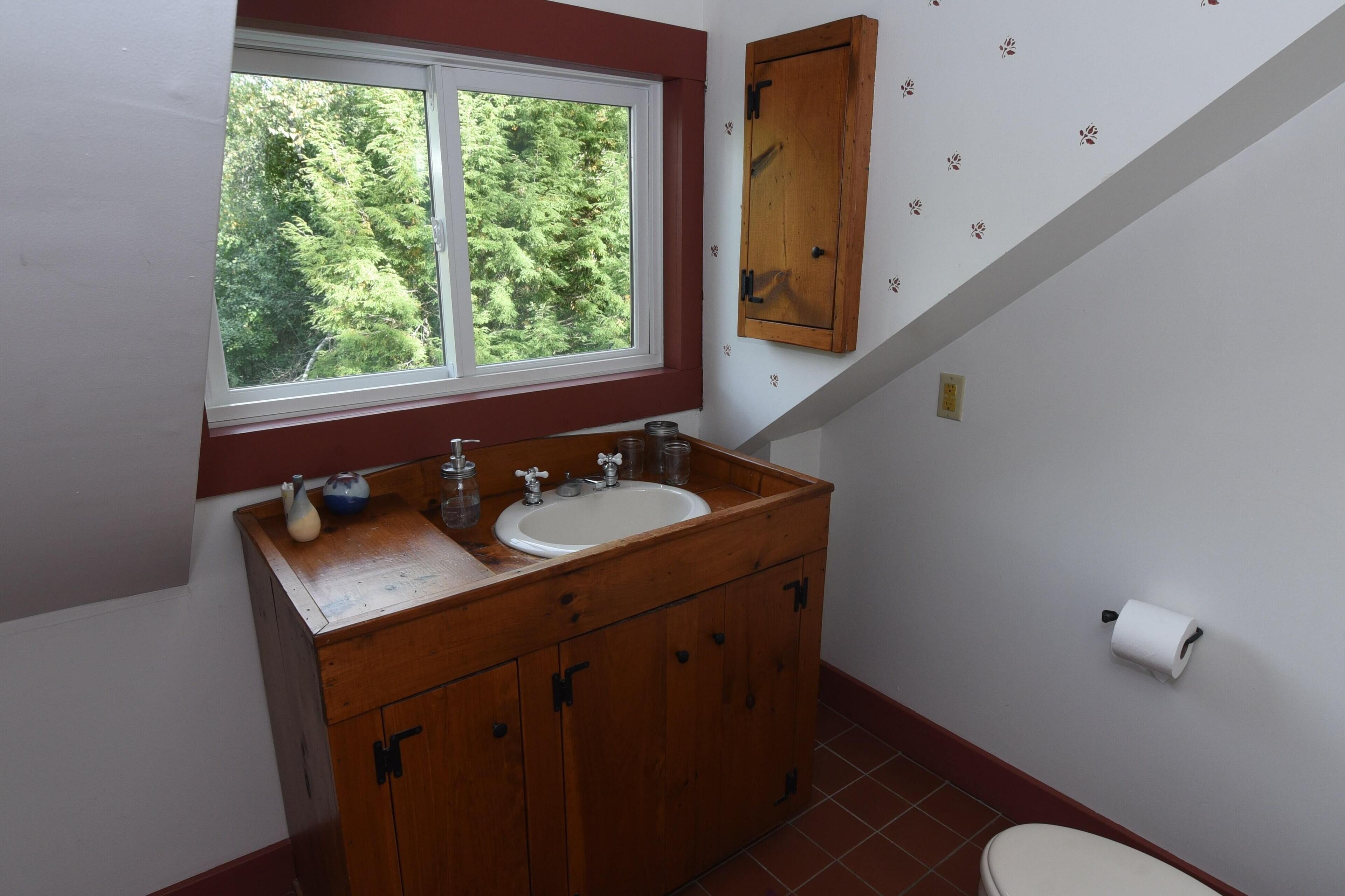 A bathroom with a wooden vanity, a window, and a toilet.