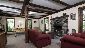 Una sala de estar acogedora con chimenea de piedra, vigas de madera y sillones rojos.