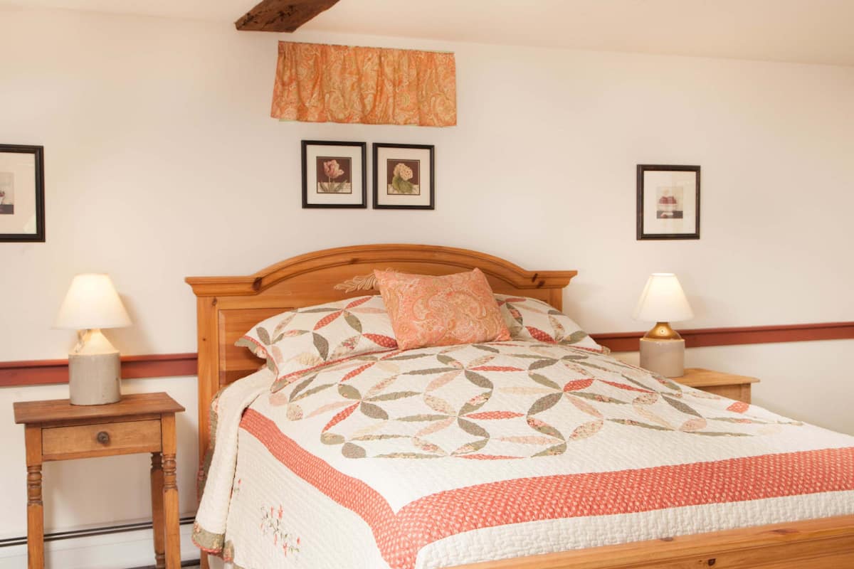 A neatly made bed with a patterned quilt, two bedside lamps, and framed pictures on the wall.