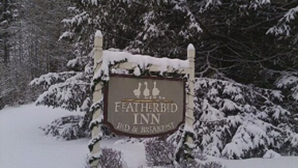 Señal del Featherbed Inn con un diseño rústico, rodeado de árboles cubiertos de nieve.