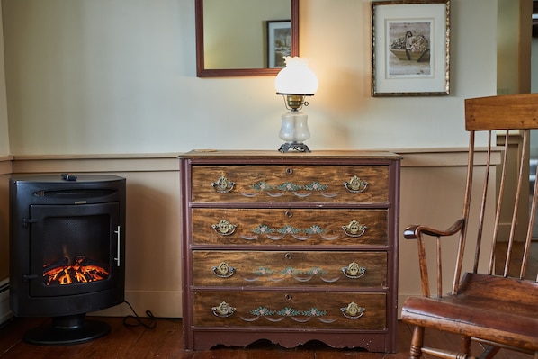 A room with a wood-burning stove, a dresser with decorative handles, and a chair. - The Featherbed Inn & Nordic Spa (Waitsfield)