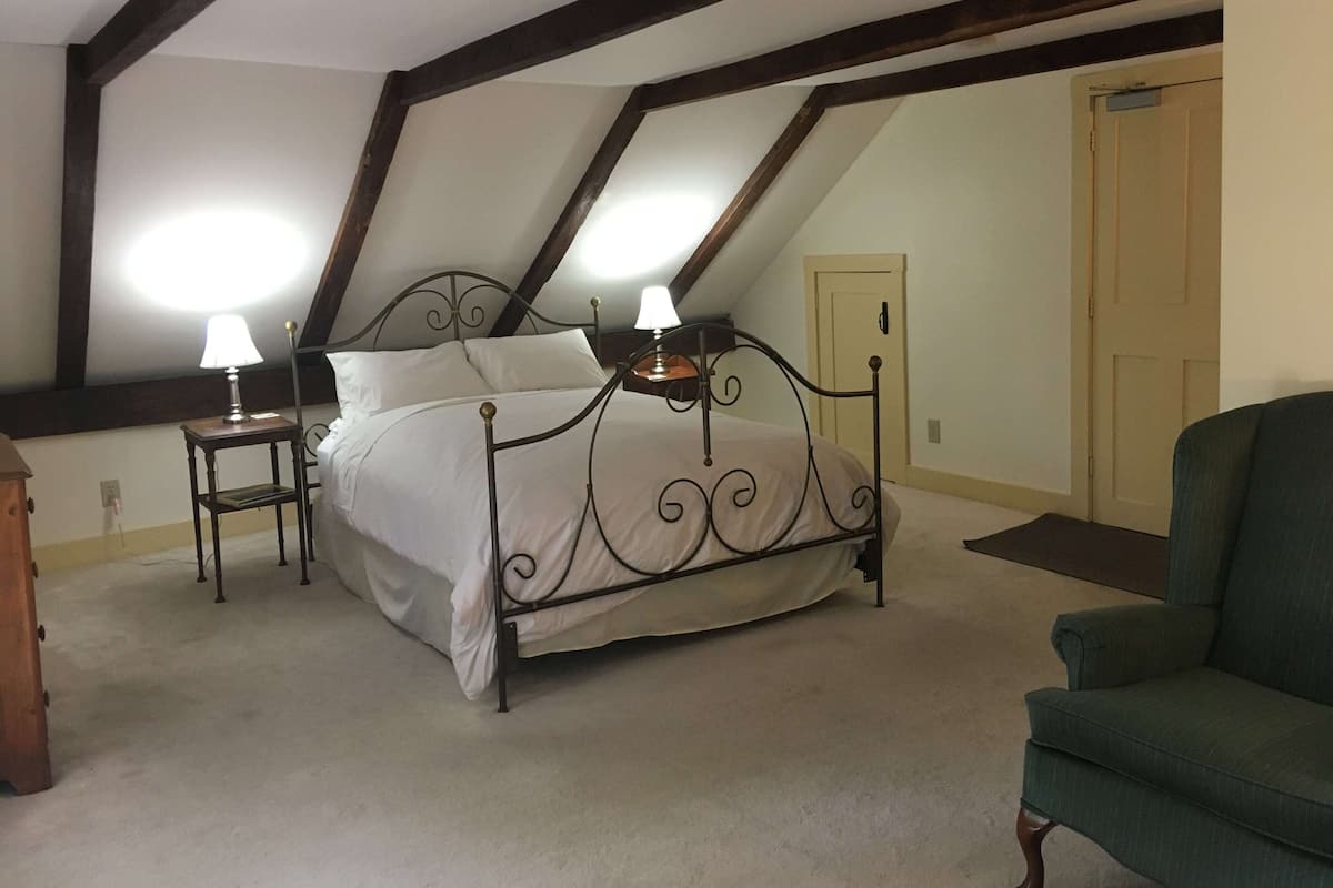 A bedroom with a bed, two bedside tables, a chair, and a door.