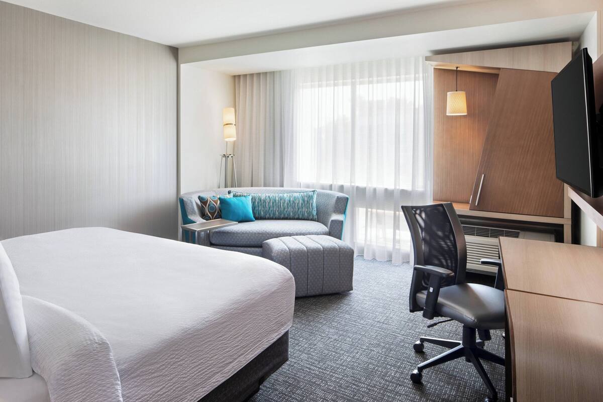 A hotel room with a large bed, a sofa, a desk, and a TV.