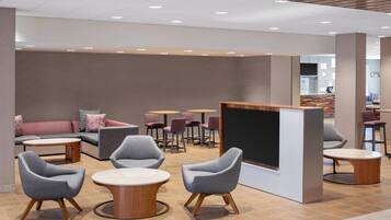 A modern lounge area with sofas, round tables, and a large screen.