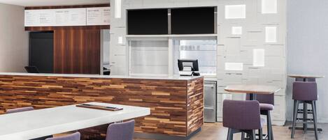 A modern cafe with a wooden counter, white tables, and purple chairs.