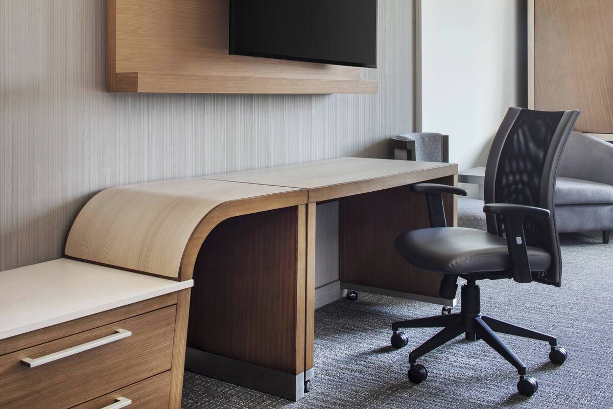 A modern office desk with a curved design, a mounted television above, and a black office chair.