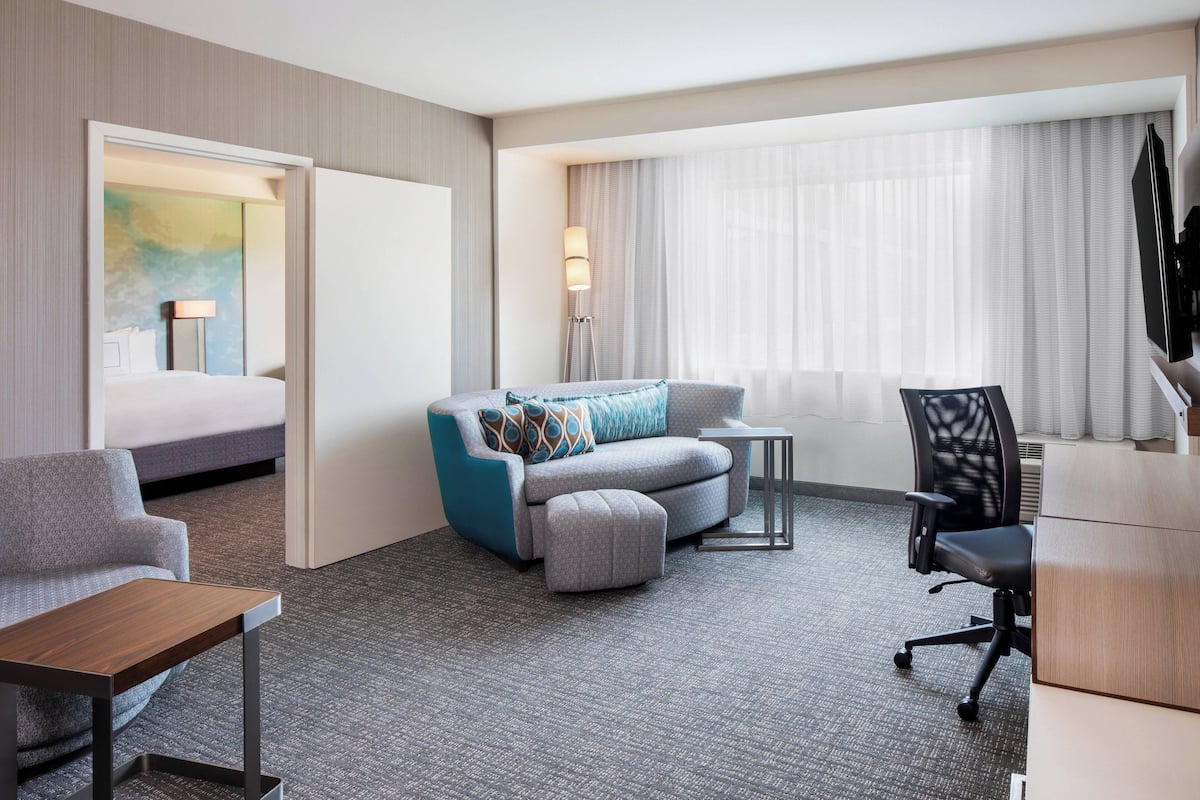 A hotel room with a bed, a sofa, a desk, a chair, and a lamp.