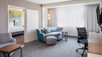 A hotel room with a bed, a sofa, a desk, a chair, and a lamp.