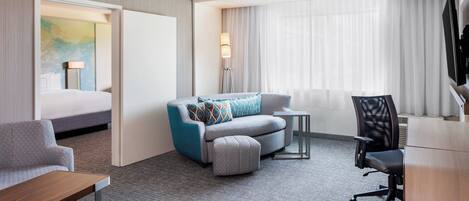 A hotel room with a bed, a sofa, a desk, a chair, and a lamp.